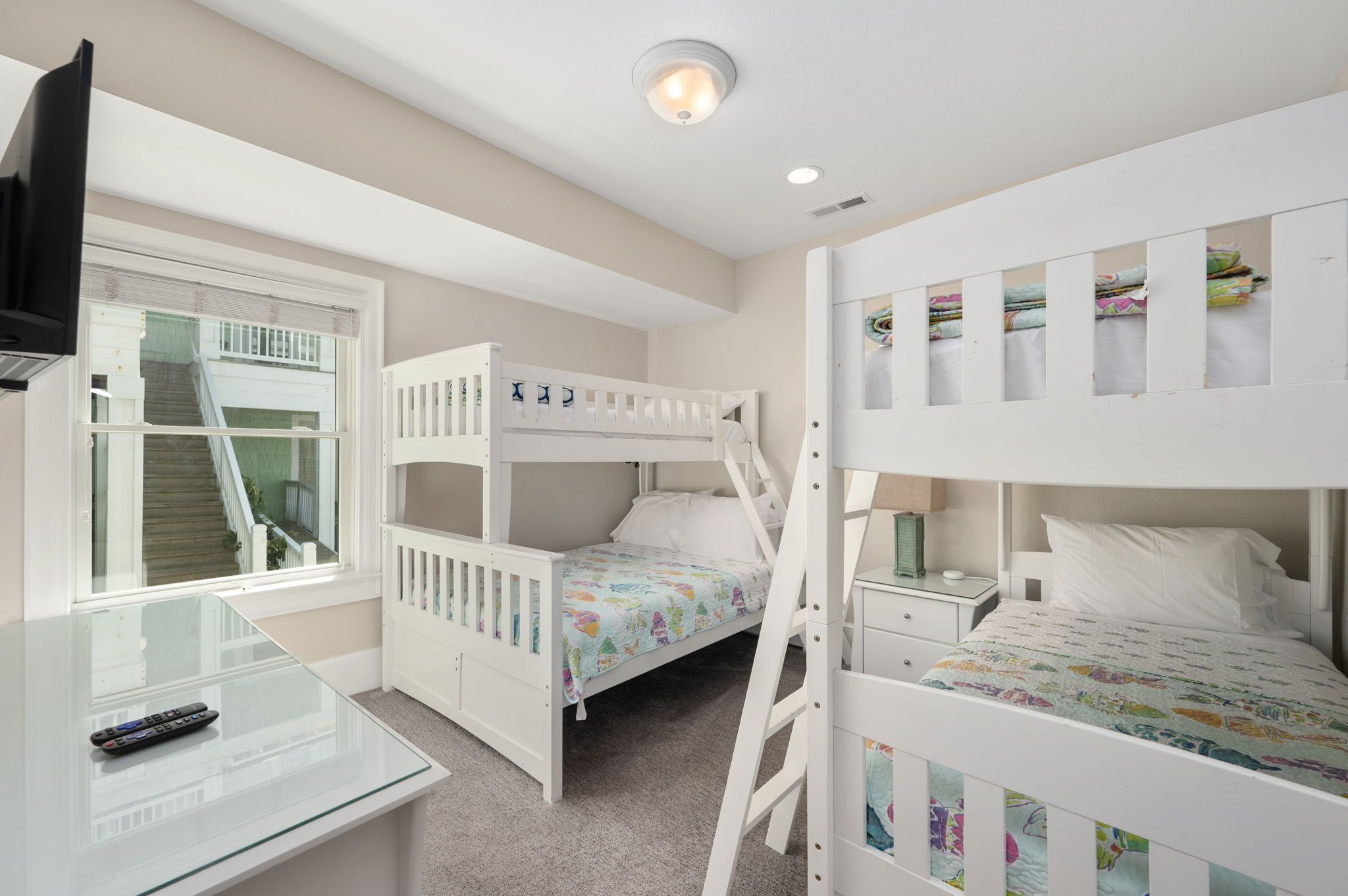 A bunk bed room with a glass desk and a television.