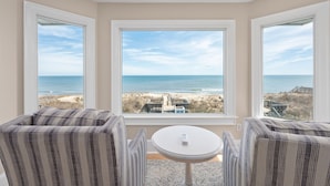 A corner room with a large window overlooking the beach, a small round table, and striped upholstered chairs. - One of These Nights: Ocean views, private pool & hot tub, rec room & elevator! (Nags Head)