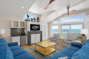 A spacious living room with a large window, a ceiling fan, and a kitchen area with white cabinets and a TV.
