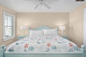 A bedroom with a bed, two bedside lamps, a ceiling fan, and a window with blinds.