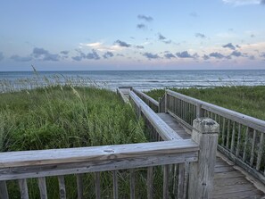A wooden boardwalk leading to the ocean with grassy areas on either side.