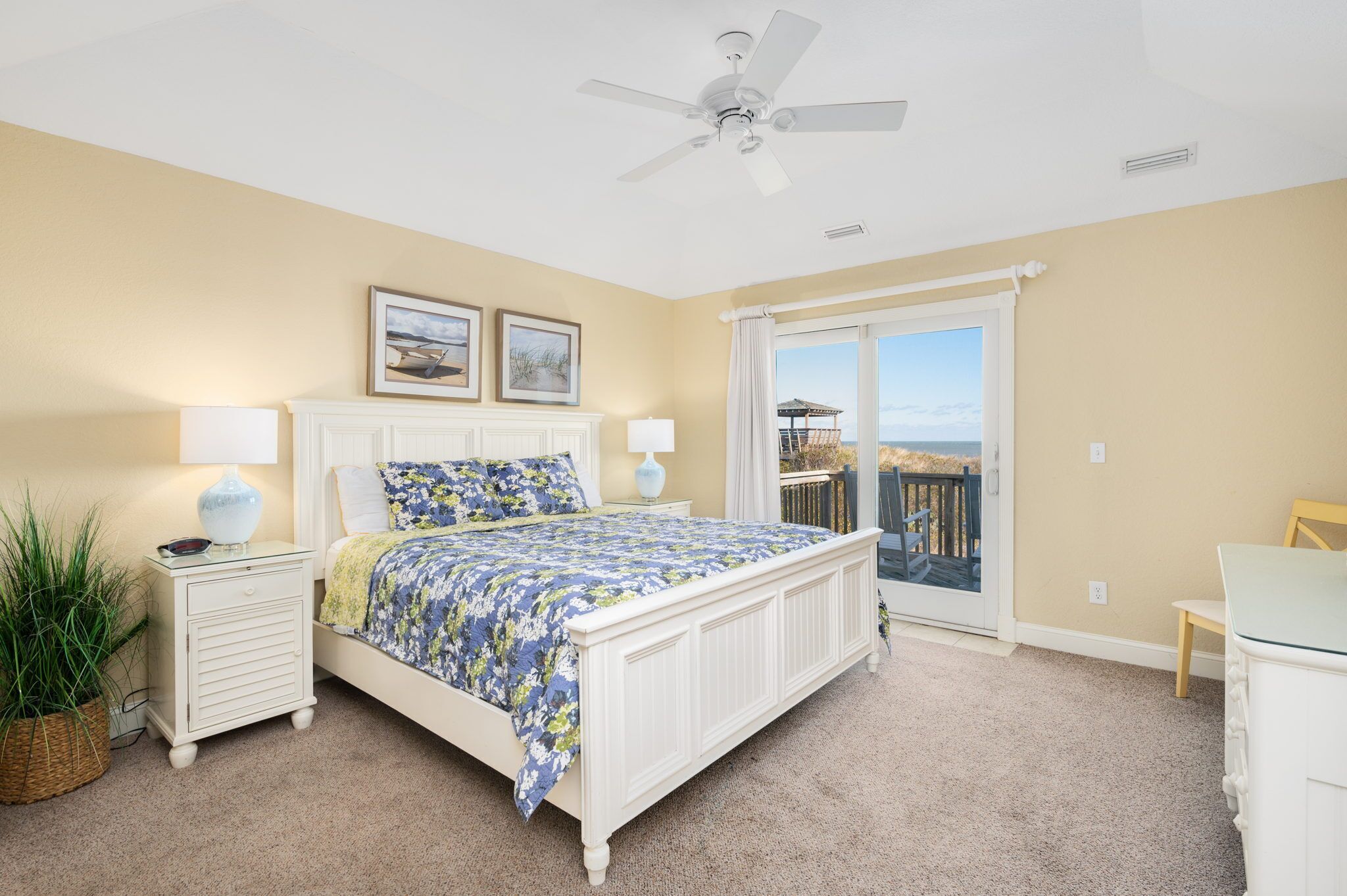 A bedroom with a bed, nightstands, a ceiling fan, a window with a view, and a balcony.