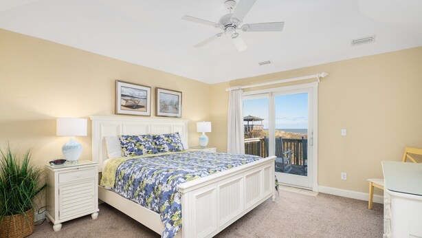Une chambre à coucher comprenant un lit, des tables de chevet, un ventilateur de plafond, une fenêtre avec vue et un balcon.