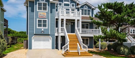 A two-story house with a front garage, a staircase leading to the second floor, and a sign for a business on the left.