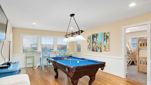 Une table de billard dans une pièce au plancher en bois, avec un canapé bleu et une table à manger entourée de chaises.