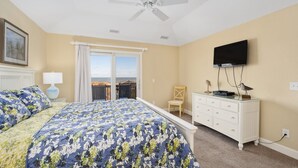Une chambre à coucher avec un lit, un ventilateur de plafond, une télévision, une commode et une fenêtre donnant sur un beau paysage.