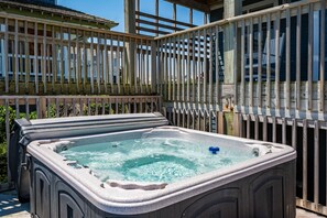 A hot tub in an outdoor setting with a wooden fence and a building in the background. - Tequila Sunrise-Oceanfront w/views, private pool, hot tub, rec room w/pool table (Nags Head)