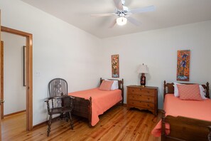 A bedroom with two single beds, a wooden chair, a nightstand, a lamp, and a ceiling fan.