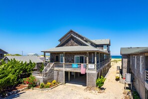 A wooden beach house with a balcony, a flag, and a sign indicating it's a vacation rental.