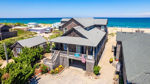 A beachfront property with multiple buildings, including a prominent house with a balcony and an American flag. - Gillam Hall: Oceanfront, private walkway, tons of space and beautiful beaches. (Nags Head)