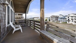 A wooden deck with a railing, white plastic chairs, and a view of residential buildings. - Phelps Brothers-Ocean Views, pool, hot tub, dog friendly, rec room & elevator! (Nags Head)