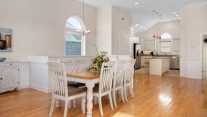 A spacious kitchen with white cabinetry, a wooden dining table, and a large island. - Phelps Brothers-Ocean Views, pool, hot tub, dog friendly, rec room & elevator! (Nags Head)