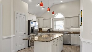 A kitchen with white cabinetry, a granite countertop island, stainless steel appliances, and pendant lighting. - Phelps Brothers-Ocean Views, pool, hot tub, dog friendly, rec room & elevator! (Nags Head)