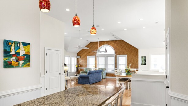A spacious kitchen with a granite countertop, a dining area with a blue sofa, and a large window with wooden shutters. - Phelps Brothers-Ocean Views, pool, hot tub, dog friendly, rec room & elevator! (Nags Head)