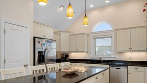 A kitchen with white cabinets, a granite countertop, a refrigerator, a coffee maker, and a dishwasher. - Phelps Brothers Too:Ocean Views, Private pool, hot tub, elevator & Dog Friendly! (Nags Head)