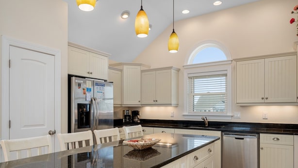 A kitchen with white cabinets, a granite countertop, a refrigerator, a coffee maker, and a dishwasher.
