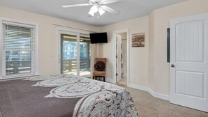 A bedroom with a bed, ceiling fan, TV, and a door leading to a balcony.