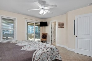 A bedroom with a bed, ceiling fan, TV, and a door leading to a balcony.