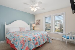 Une chambre à coucher avec un lit, un ventilateur de plafond, une fenêtre avec des stores et une chaise.
