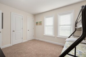 A bedroom with a bunk bed, two white doors, and two windows with blinds.