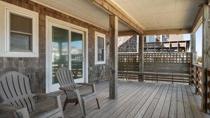 Katettu kuisti, jossa on Adirondack-tyyliset puutarhatuolit, puinen terassi ja näkymä takapihalle.