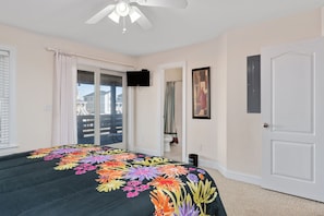 Une chambre à coucher avec un lit, un ventilateur de plafond, une télévision, une porte et une vue sur l’extérieur.
