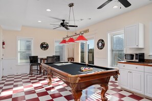 Une table de billard avec un sol à carreaux, un ventilateur de plafond et un four à micro-ondes dans le coin cuisine.