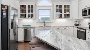 A modern kitchen with white cabinetry, a marble countertop, and a built-in oven. - Phelps: Semi-oceanfront w/private pool, hot tub, rec and media room & elevator! (Nags Head)