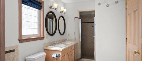 A bathroom with two sinks, a toilet, a shower, and a window with a blue curtain.