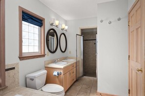 Un baño con dos lavamanos, un inodoro, una ducha y un ventanal con cortina azul.