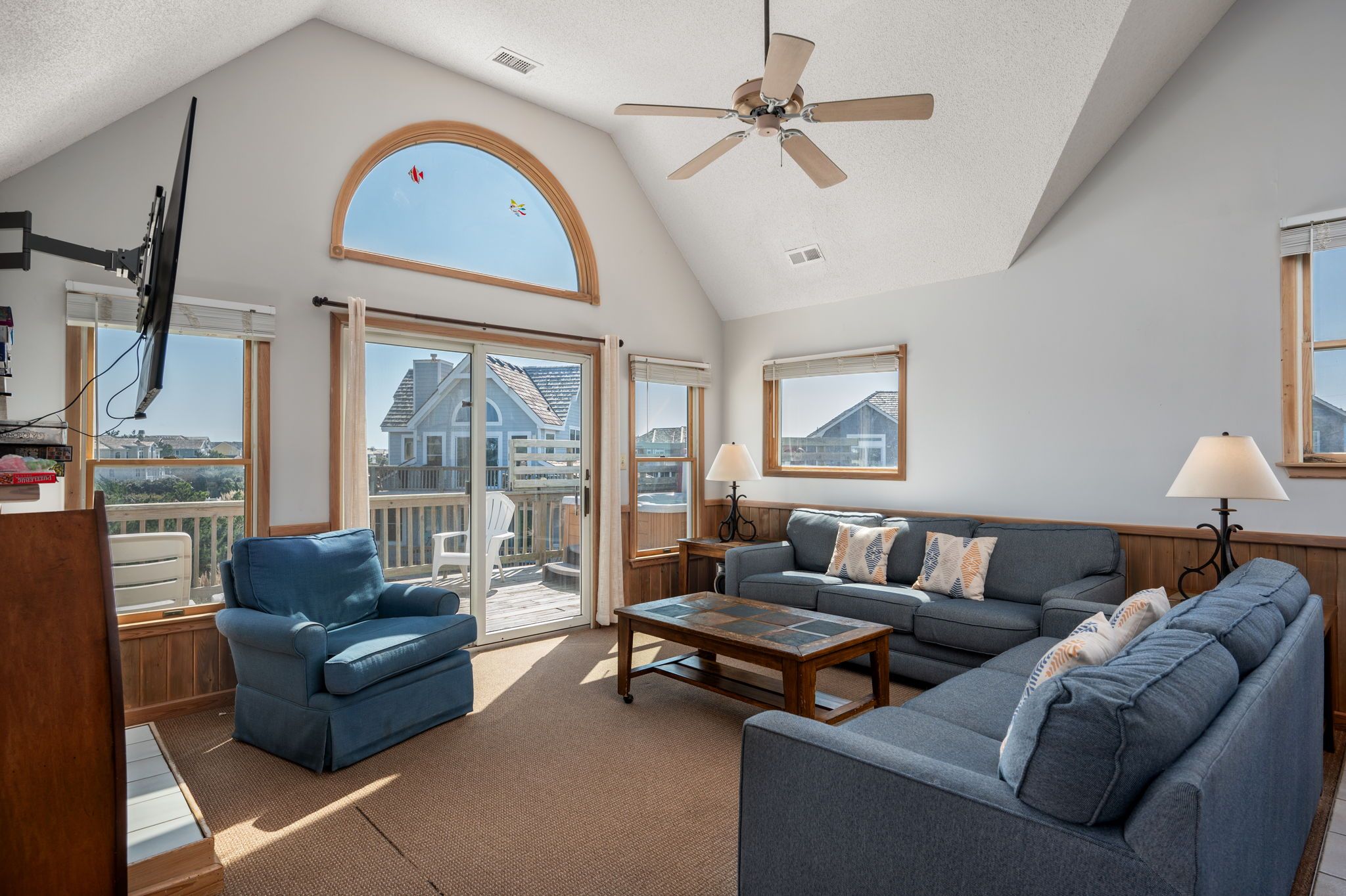 A spacious living room with a high ceiling, a ceiling fan, a large window with a view, and a sliding glass door leading to an outdoor area.