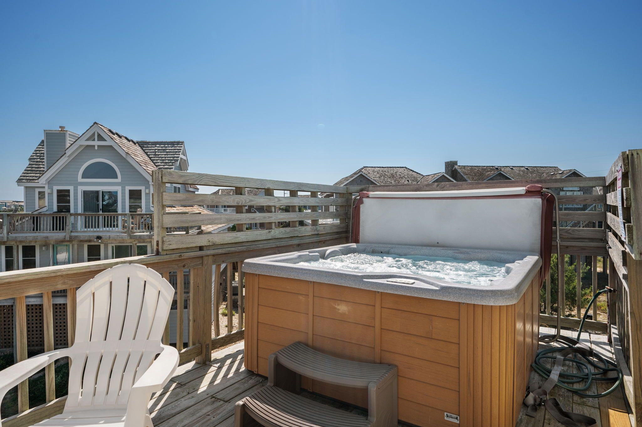 A wooden deck with a hot tub, a white chair, and a wooden bench.