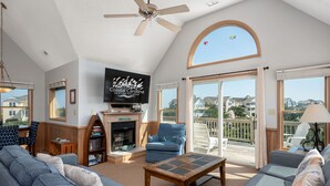 Amplia sala de estar con chimenea, televisor y un balcón con vistas a casas.