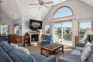 A spacious living room with a fireplace, a television, and a balcony with a view of houses.