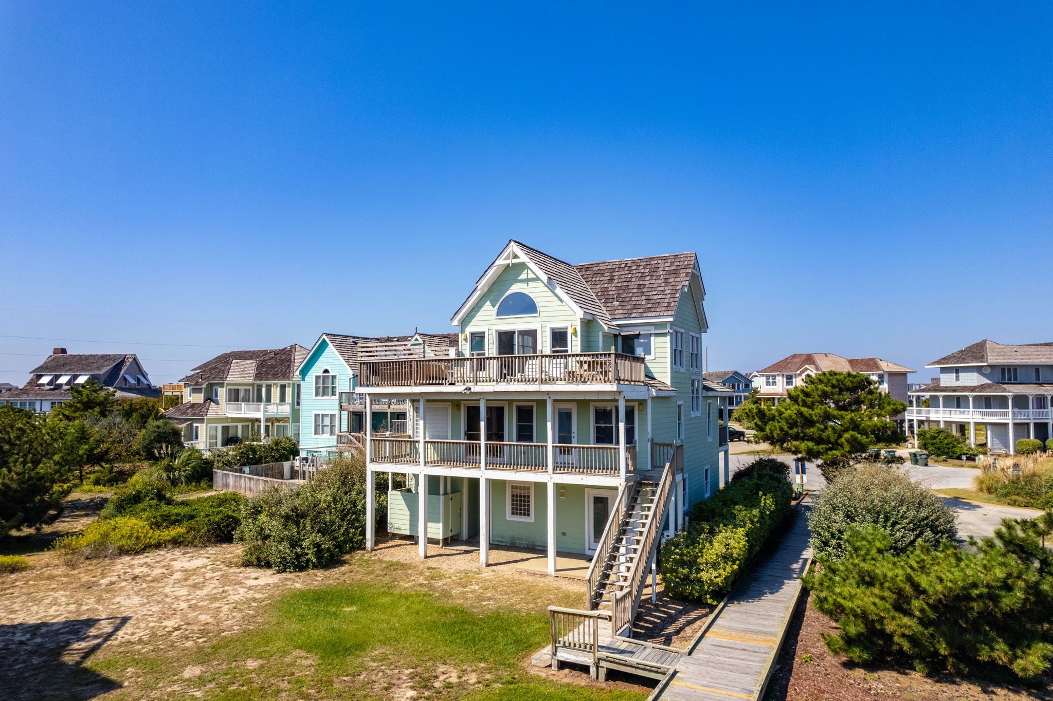Ein mehrstöckiges Strandhaus mit Balkon, einer Treppe, die zum Obergeschoss führt, und einer Holzterrasse.