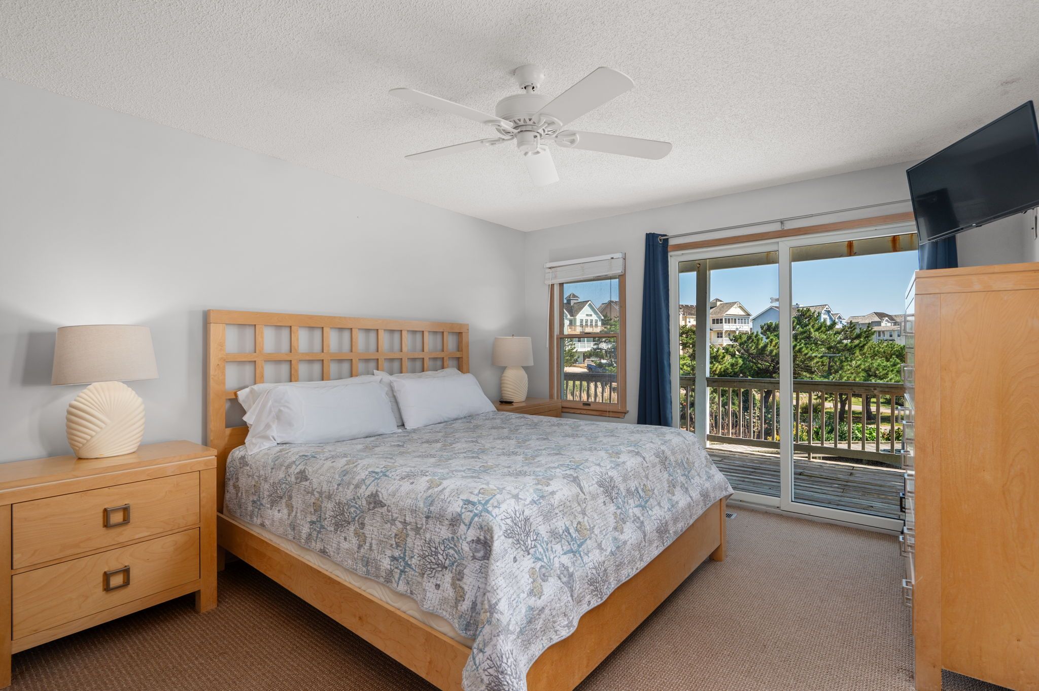 Un dormitorio con cama de madera, mesita de noche, ventilador de techo y vistas al balcón exterior.