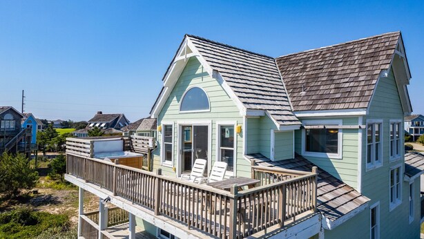 Ett ljusgrönt hus med en balkong, en inglasad uteplats och utsikt över det omgivande bostadsområdet.