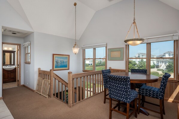 A dining area with a round table and chairs, a staircase with a wooden railing, and a view of houses through large windows.