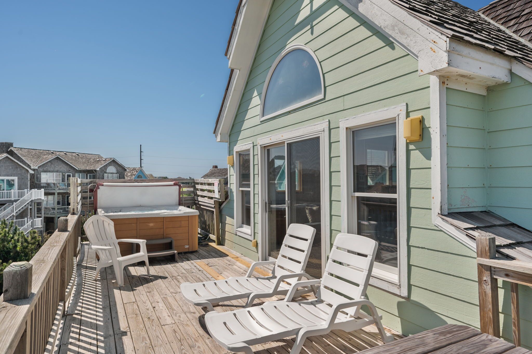 A deck with two white lounge chairs, a wooden table, and a glass-enclosed patio area.