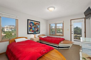 A bedroom with two beds, a painting, and a TV. - Newwinds Hideaway-Semi-oceanfront, community pool, private hot tub, ocean views, dog friendly! (Nags Head)
