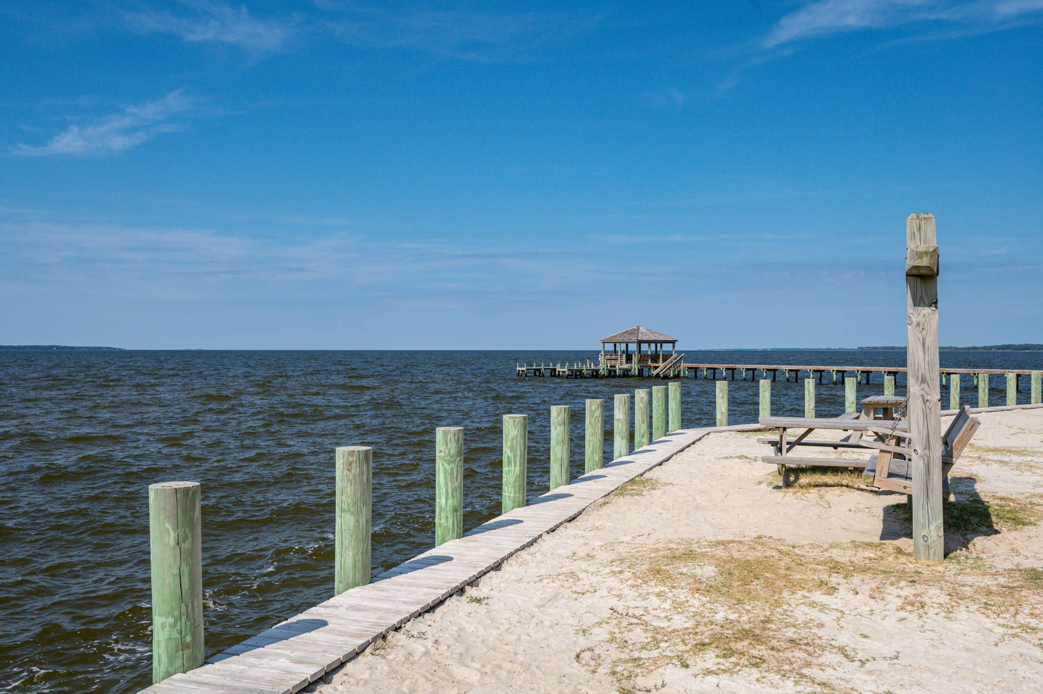 A wooden pier extending into a body of water with a small gazebo and picnic tables at the end.