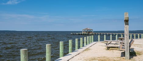 Un muelle de madera se extiende sobre el agua, con un pequeño pabellón y mesas de picnic al final.