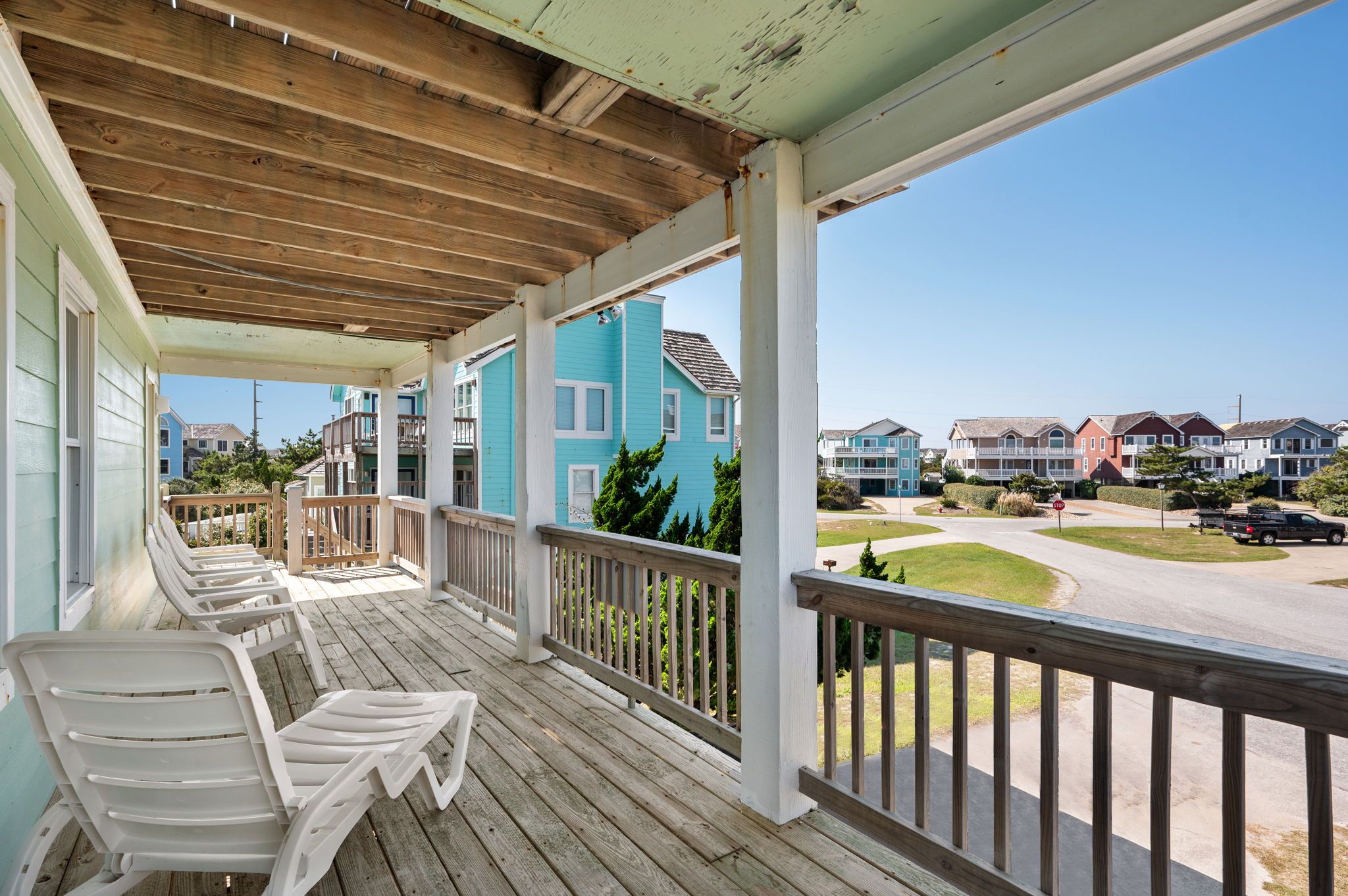 A covered porch with white plastic chairs, a wooden ceiling, and a view of colorful townhouses.