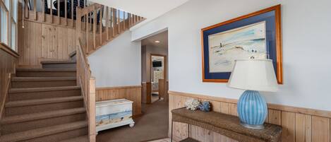 Un escalier avec des rampes en bois menant à un palier, un tableau encadré accroché au mur et une console en osier sur laquelle est posée une lampe.