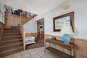 A staircase with wooden railings leading to a landing, a framed painting on the wall, and a wicker console table with a lamp.