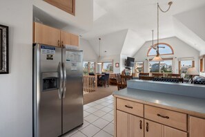 A spacious kitchen with a large refrigerator, wooden cabinets, and a dining area with a view of the outside. - Newwinds Hideaway-Semi-oceanfront, community pool, private hot tub, ocean views, dog friendly! (Nags Head)
