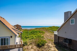 A coastal property with a view of the ocean, a wooden deck, and a grassy area. - At Ease: Ocean views, short walk to the beach, close to fishing pier. (Nags Head)