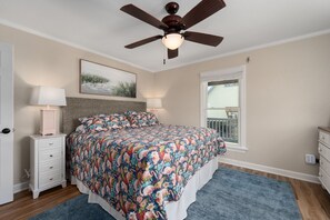Un dormitorio con cama, ventilador de techo, ventana y mesita de noche.