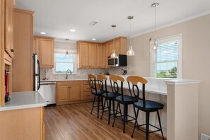 A kitchen with wooden cabinets, a microwave, a sink, and bar stools. - At Ease: Ocean views, short walk to the beach, close to fishing pier. (Nags Head)