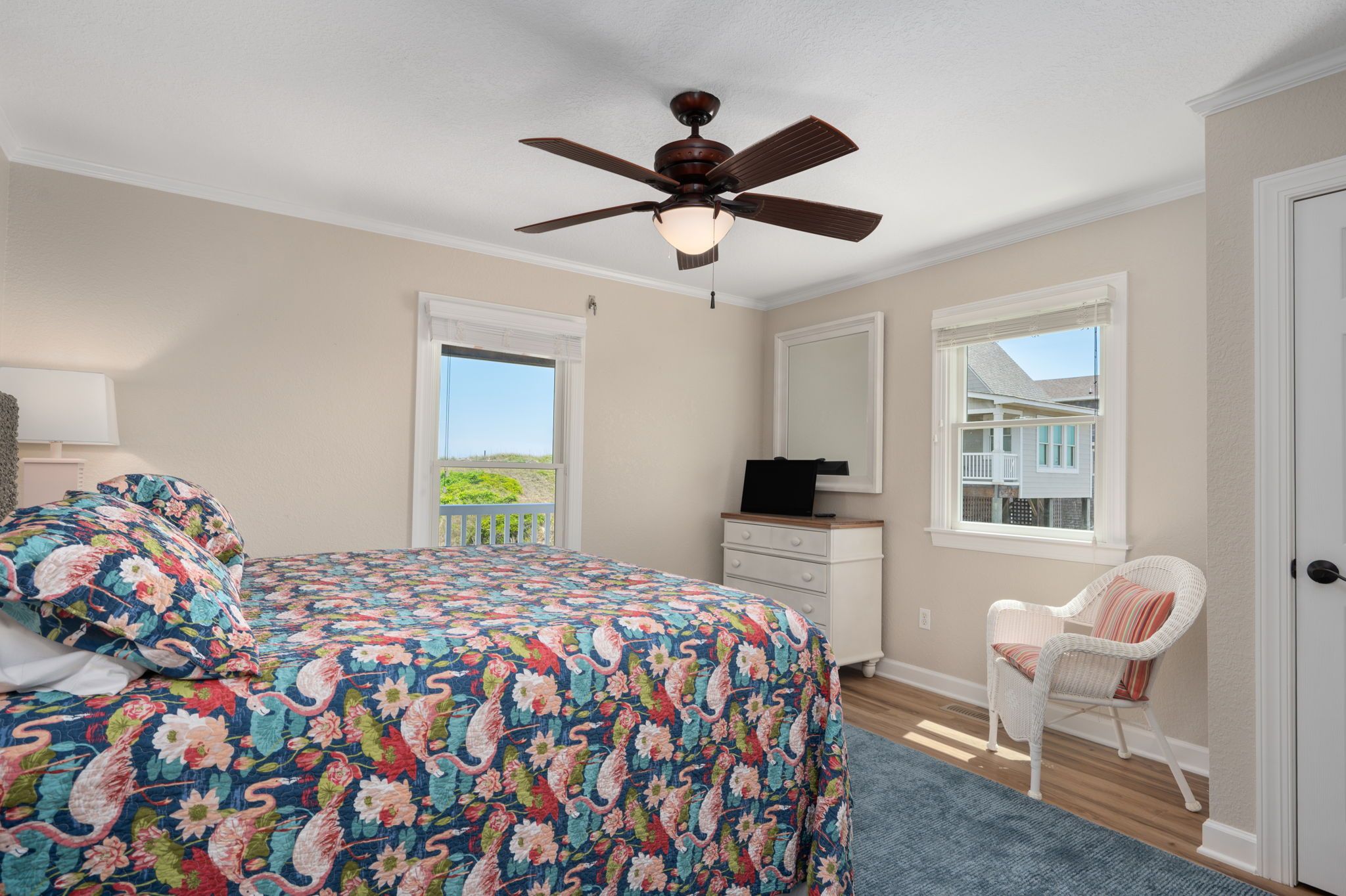 A bedroom with a bed, a ceiling fan, a dresser, a chair, and a window with a view.